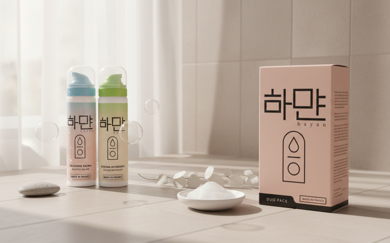 Kit cura tatuaggi Hayan: Soluzione Salina (flacone ciano) e Schiuma Detergente (flacone verde) esposti dinamicamente con la scatola Duo Pack. Fotografia professionale in studio con illuminazione mirata e tonalità neutre.