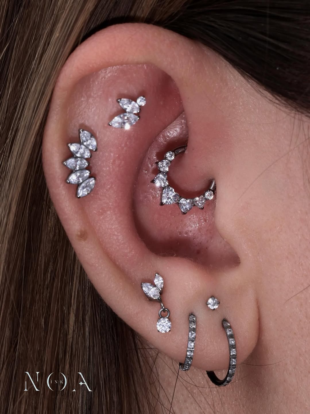 Orecchio con multipli piercing con gioielli in zirconia: helix, conch, lobo e tragus brillanti. curato da NOA INK
