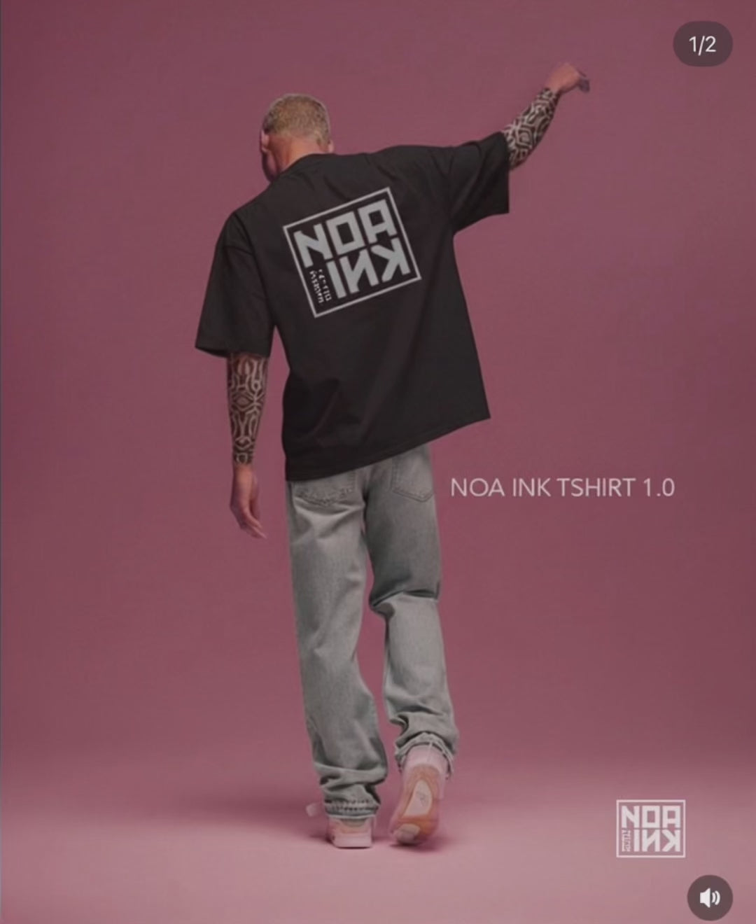 Uomo con tatuaggi indossa la Noa Ink icon drop T-Shirt nera oversize, con maxi logo quadrato bianco sul retro. Sfondo rosa minimal, look streetwear con jeans chiari e sneakers. Maglietta unisex firmata Noa Ink, dallo stile urbano e contemporaneo.