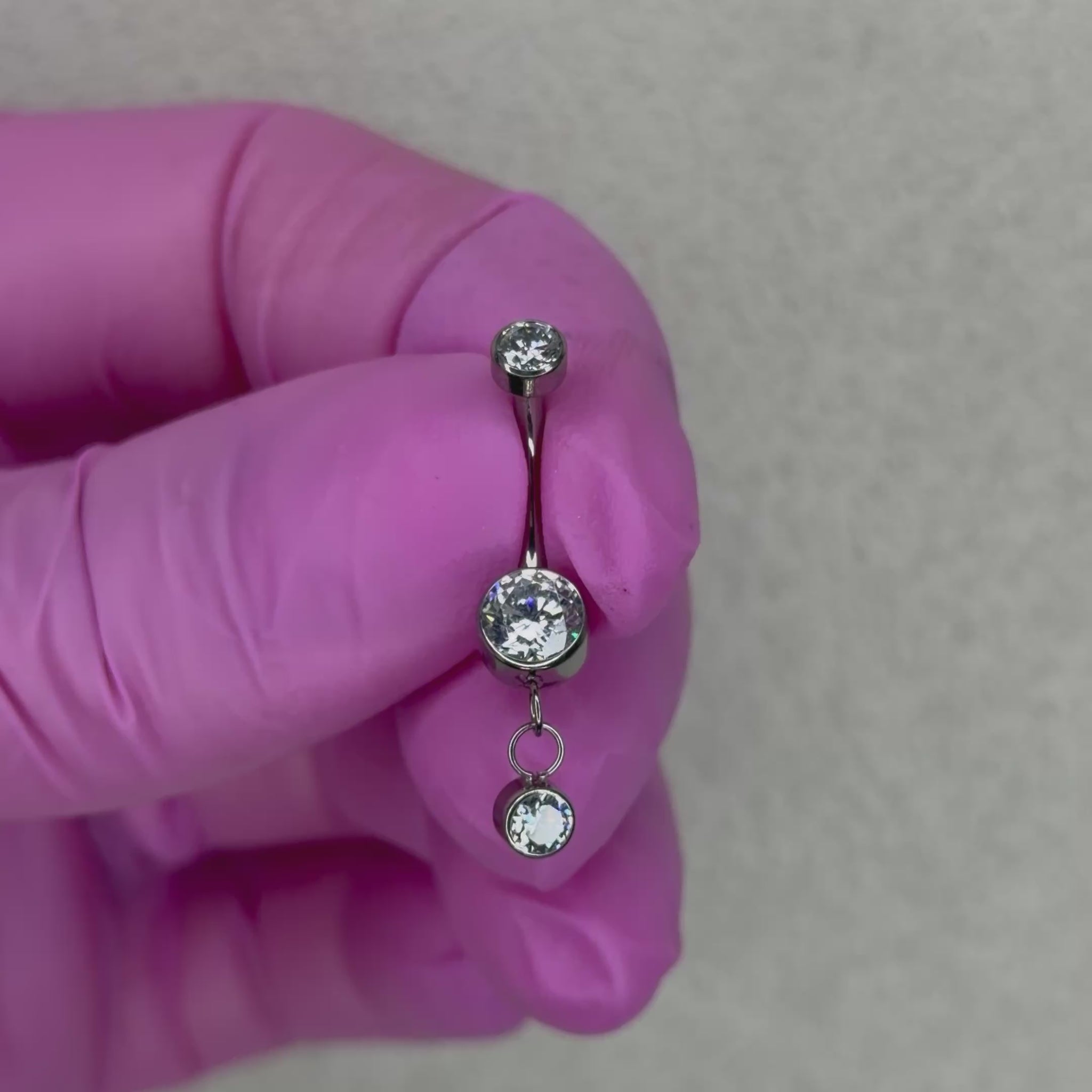 Piercing da ombelico in Titanio ASTM F136 dal design elegante e luminoso. La pietra centrale è arricchita da un delicato pendente con cristallo, creando un effetto raffinato e leggermente movimento sul piercing.
Perfetto per chi cerca un navel piercing con pendente elegante e versatile, capace di aggiungere un piccolo punto luce senza risultare eccessivo.