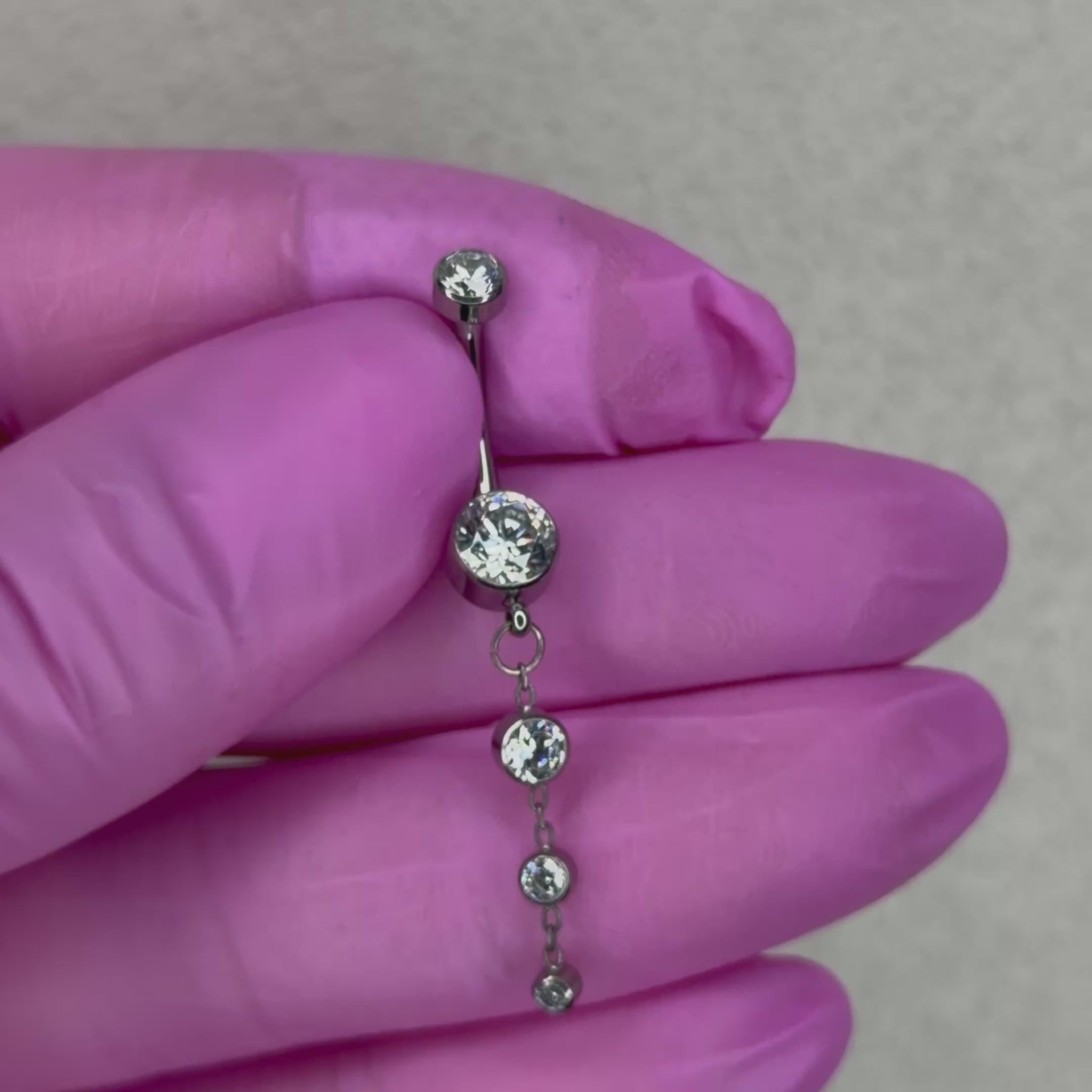 Piercing da ombelico dal design elegante e luminoso, caratterizzato da un pendant con cristalli di diverse dimensioni che crea un delicato effetto cascata. Un gioiello pensato per chi ama un navel piercing più particolare e ricco di dettagli, perfetto per aggiungere luminosità al piercing all’ombelico.